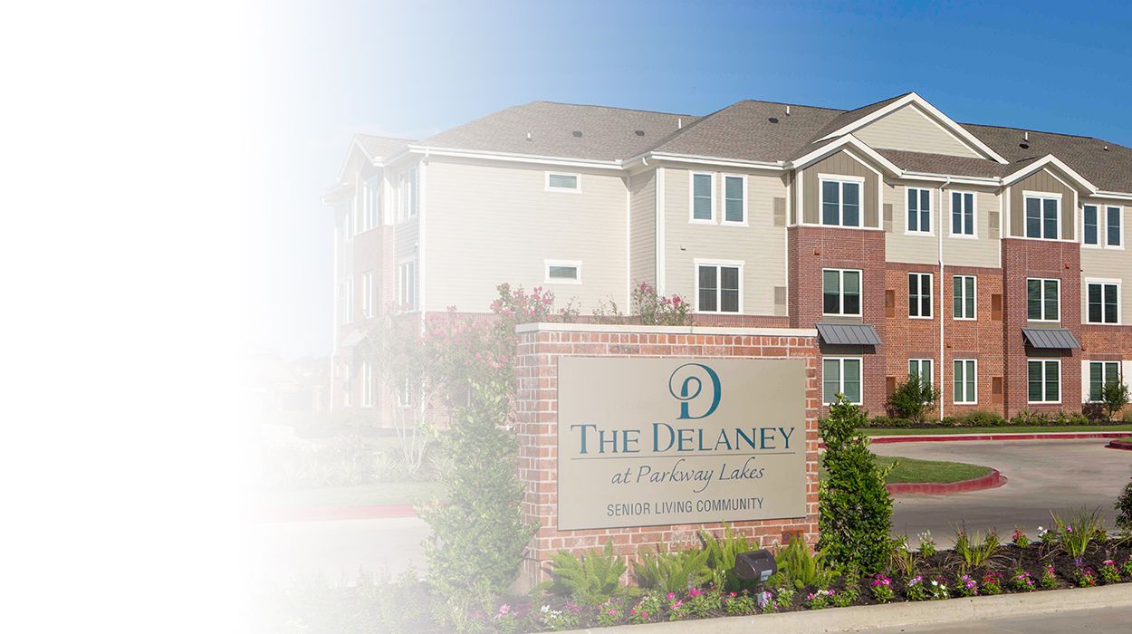 white fade outside main sign The Delaney at Parkway Lakes senior living community