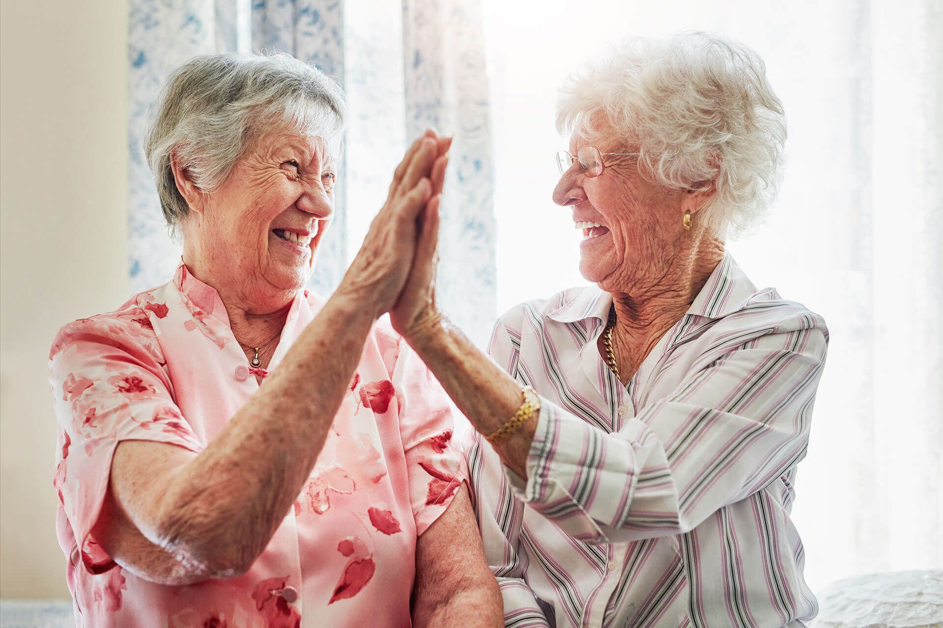 elderly women doing a high-five at The Delaney at Parkway Lakes senior living retirement community