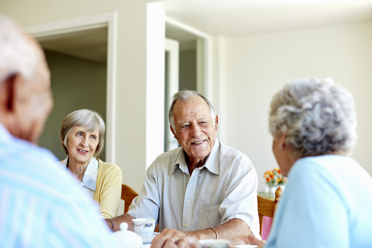 Older adults enjoying conversation around a table in a community dining area.