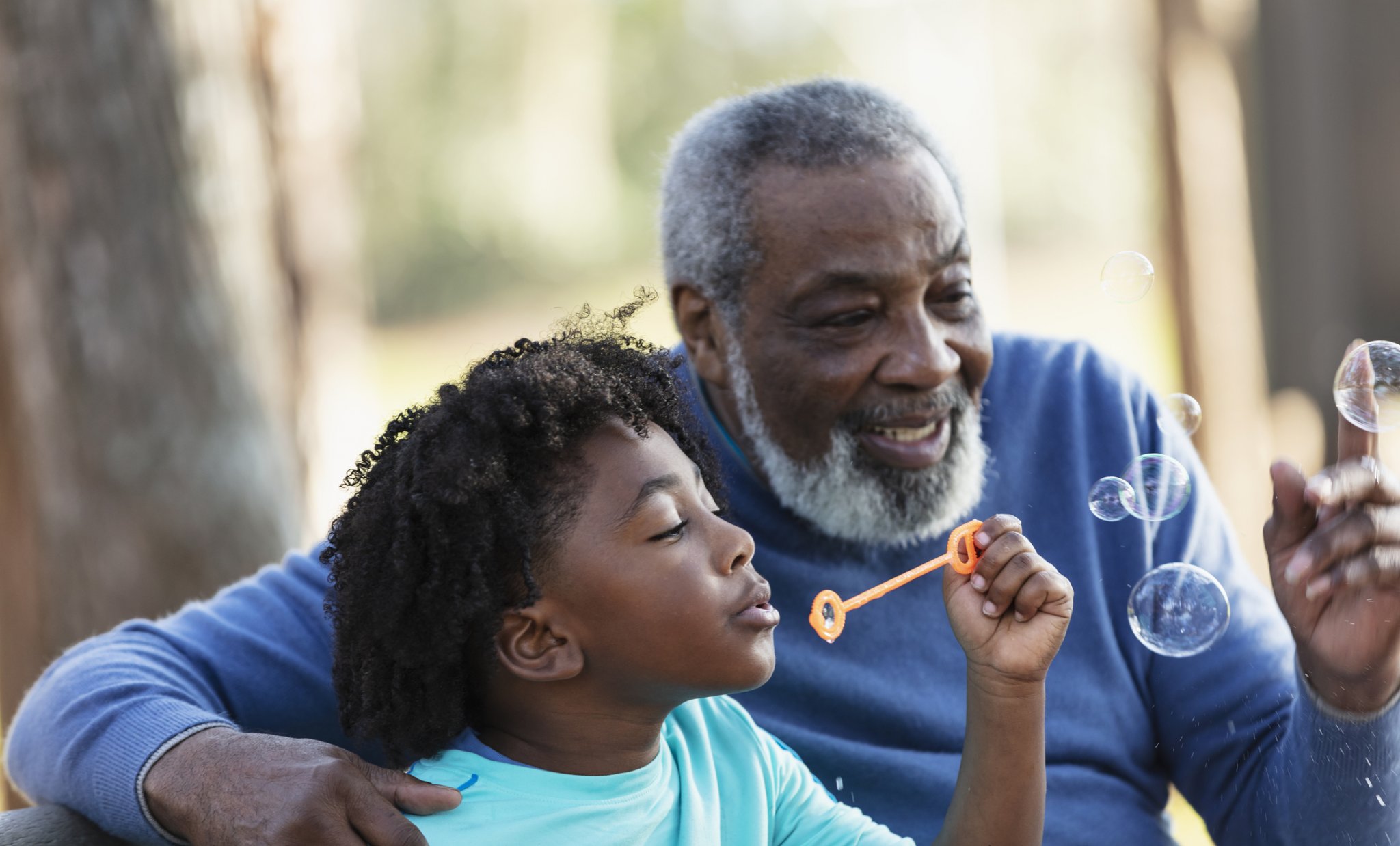 Elderly man and young boy joyfully blowing bubbles outdoors on a sunny day.