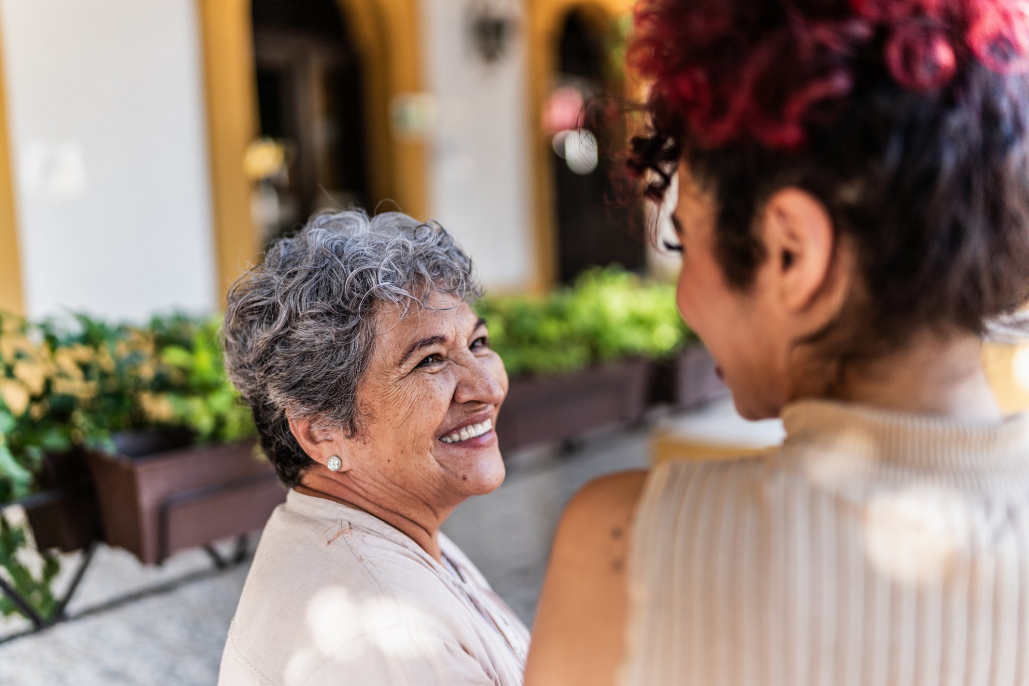 Two women sharing a joyful moment outside residential units, with greenery in the background.