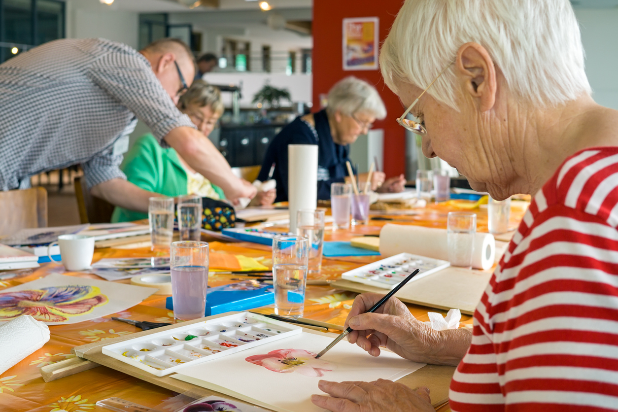 Seniors engaged in a watercolor painting class at a communal activity room.