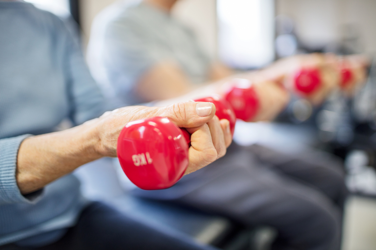 Close-up of older adults lifting small red dumbbells during an exercise class.