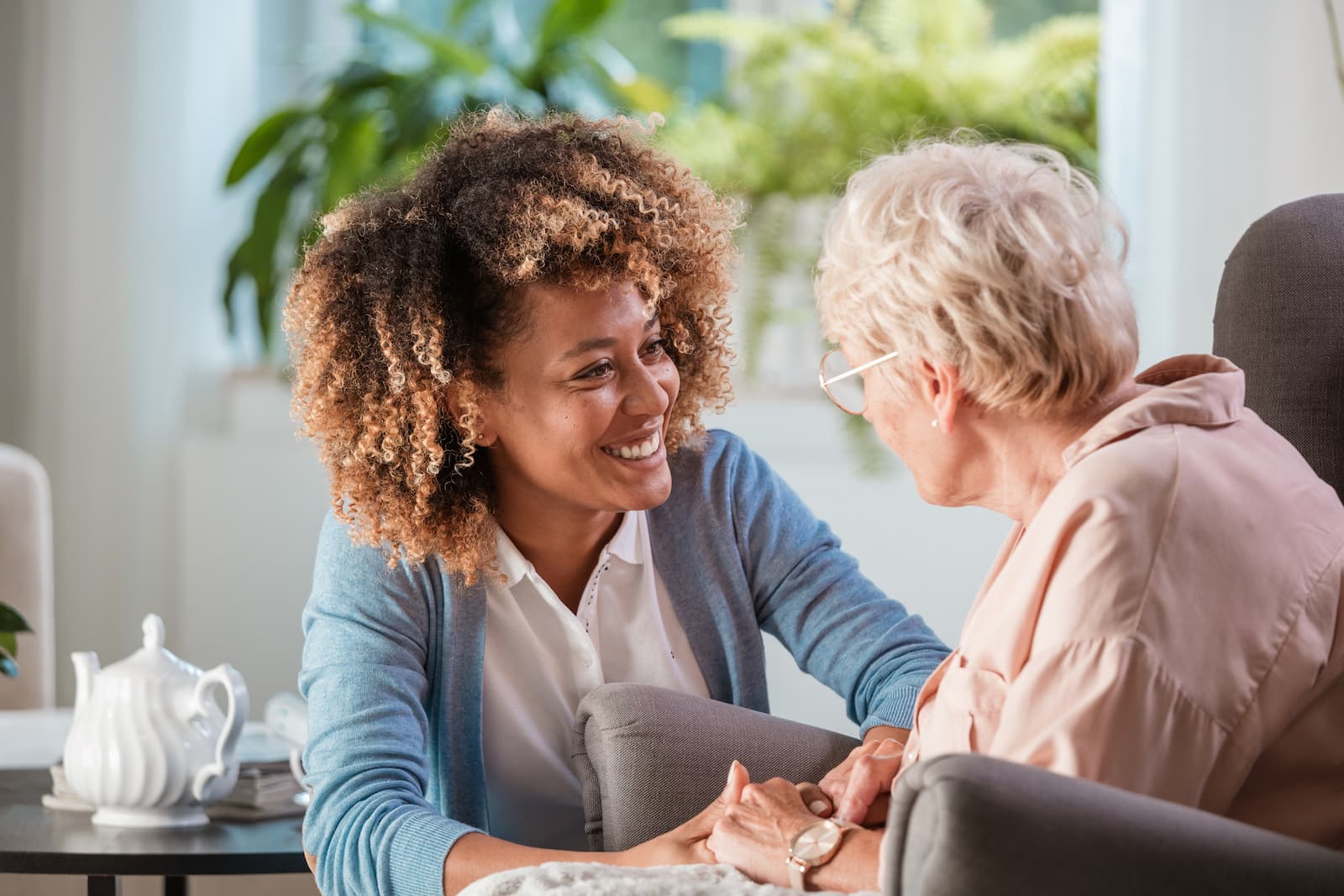 Caregiver leans in and checks on senior woman as they hold hands