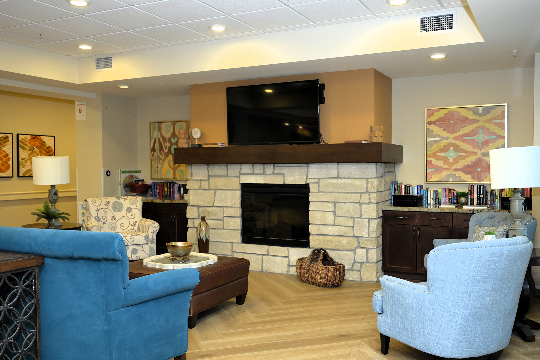 Cozy living area with stone fireplace, blue chairs, and wall-mounted TV.