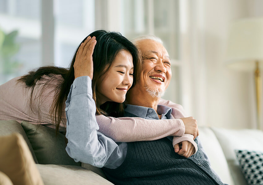 Senior man hugs adults granddaughter over his shoulder