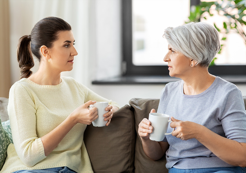 Senior woman and adult daughter sitting by lake having a conversation